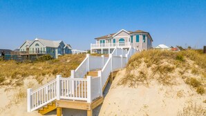 Une propriété située en bord de mer, avec un escalier en bois menant à une maison à plusieurs étages dotée de balcons.