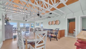 Une salle à manger spacieuse avec un plafond haut et des poutres en bois, des chaises blanches et une table en bois.