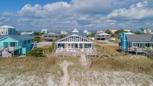 Une propriété située en bord de mer, avec un bâtiment principal doté d’une terrasse et d’un espace salon extérieur, le tout entouré de maisons de plage.