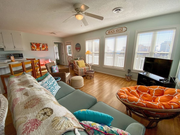 Ein Wohnzimmer mit einer Couch, Sesseln, einem Fernseher und einem Schild mit der Aufschrift 'BEACH HOUSE'.