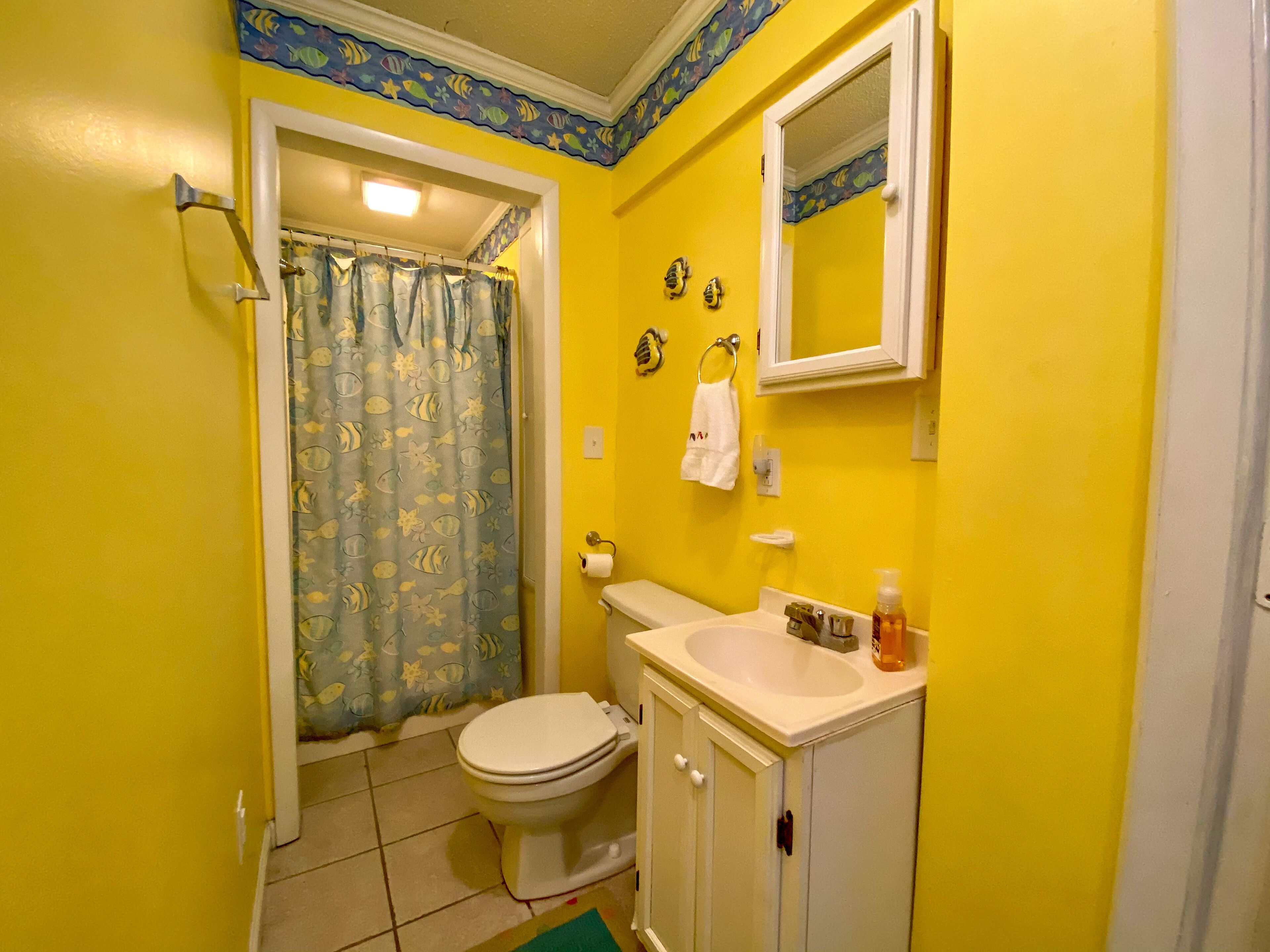 A bathroom with yellow walls, a white toilet, a sink with a mirror above it, and a shower curtain with a fish pattern.