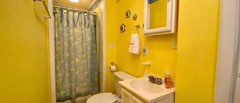 A bathroom with yellow walls, a white toilet, a sink with a mirror above it, and a shower curtain with a fish pattern.