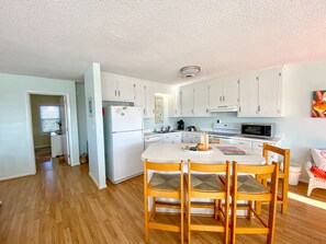 A compact kitchen with white cabinets, a central island with chairs, a refrigerator, and a microwave. - POOL and beach access steps away from driveway! (Emerald Isle)