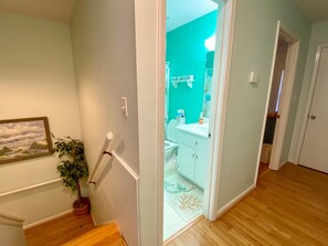 A hallway with a staircase leading to a bathroom with a turquoise wall and white cabinets. - POOL and beach access steps away from driveway! (Emerald Isle)