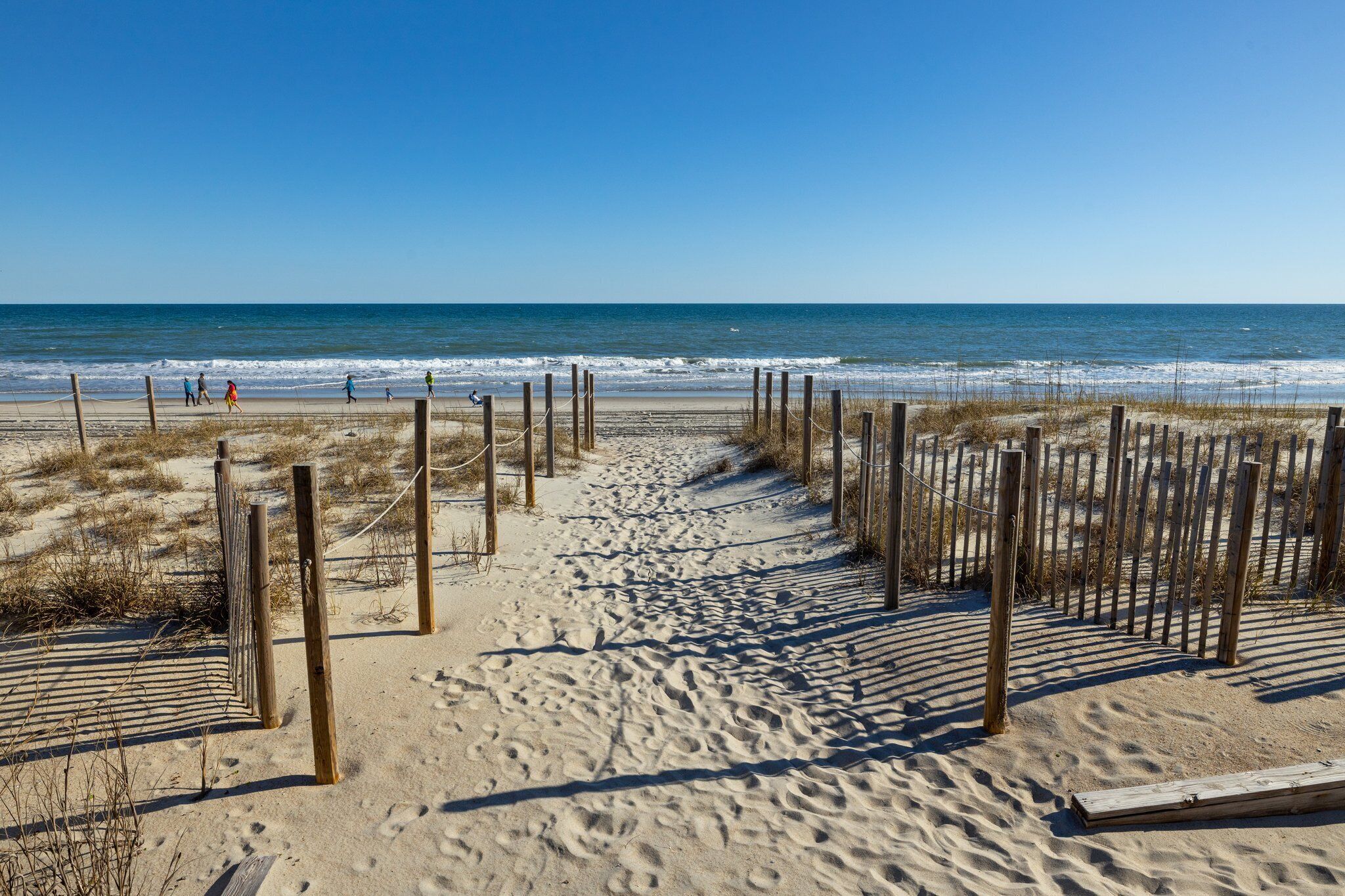 Une plage de sable avec des poteaux en bois et des cordes formant un chemin qui mène à l’océan.