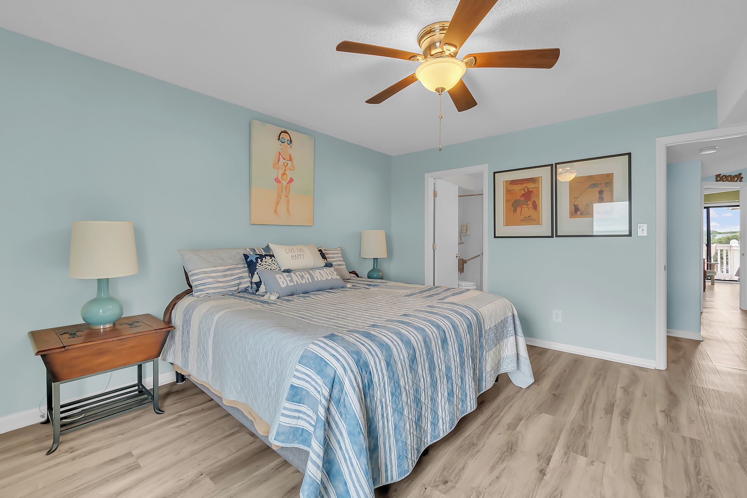 A bedroom with a bed, nightstands, a ceiling fan, and artwork on the walls.