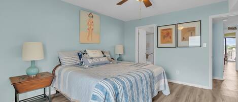A bedroom with a bed, nightstands, a ceiling fan, and artwork on the walls.