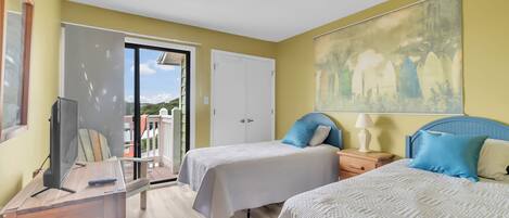 A hotel room with two beds, a desk, a TV, and a balcony with a view.