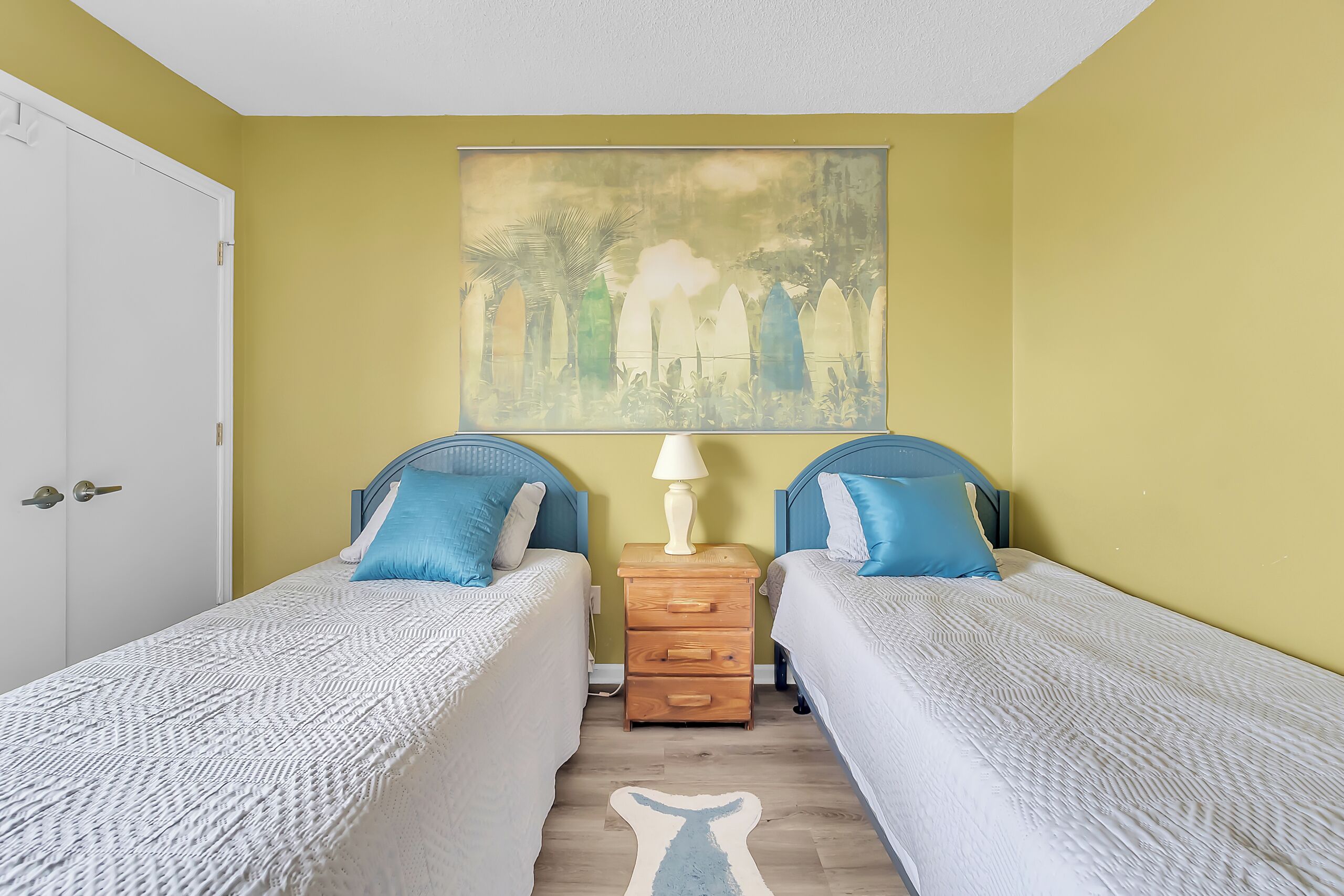A room with two single beds, a nightstand with a lamp, and a painting on the wall.