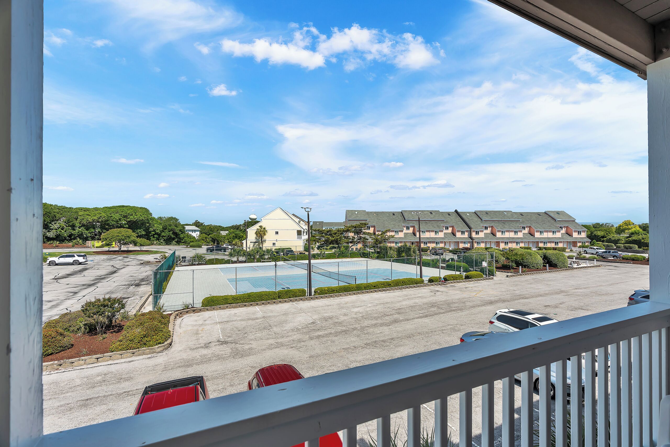 A view from a balcony overlooking a parking lot, a swimming pool, and a building with multiple floors.