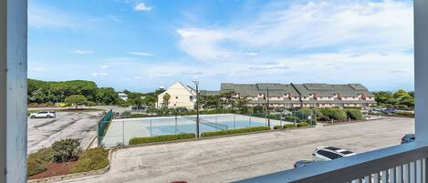 A view from a balcony overlooking a parking lot, a swimming pool, and a building with multiple floors.