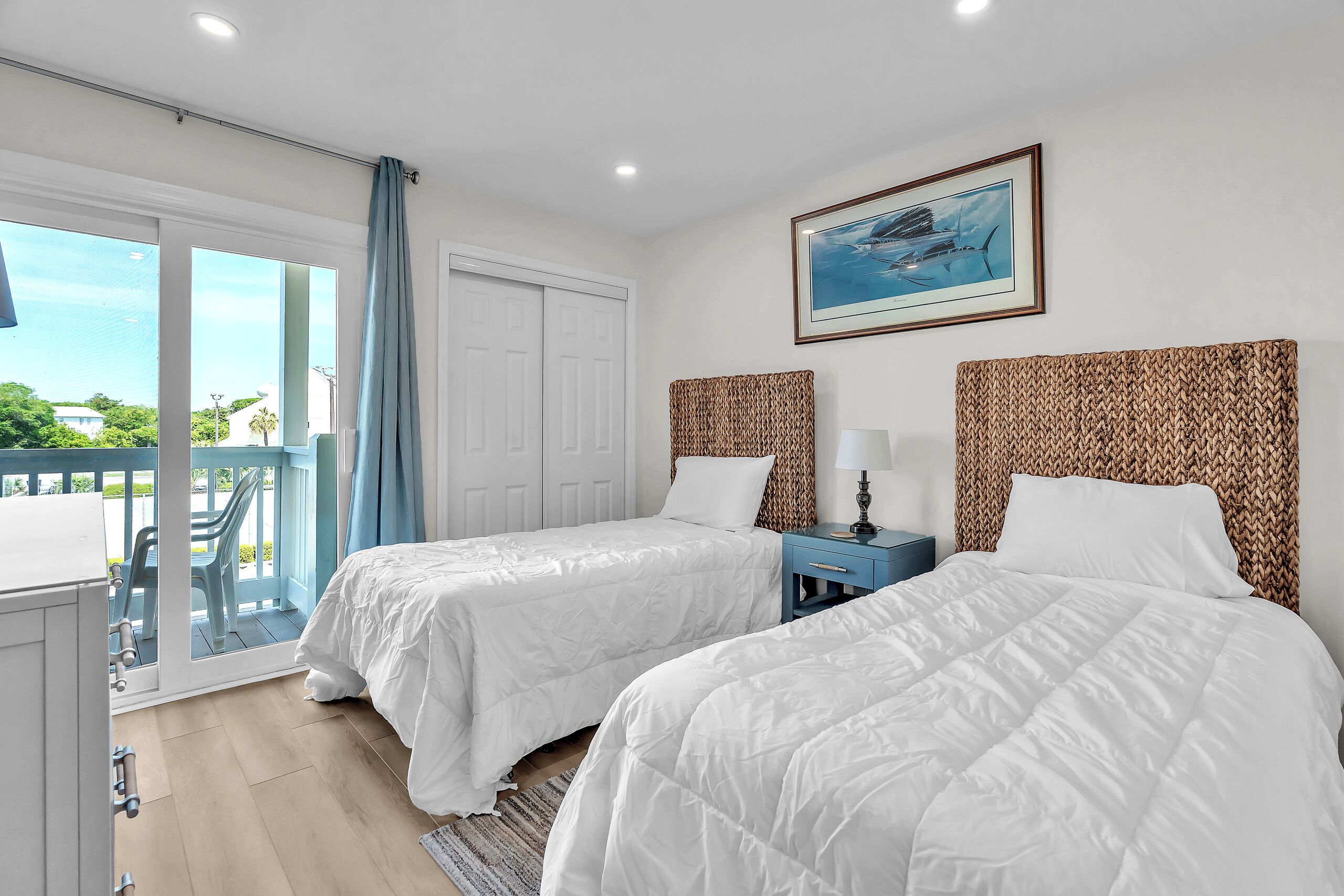 A hotel room with two beds, a balcony, a painting, and a view of the outdoors.
