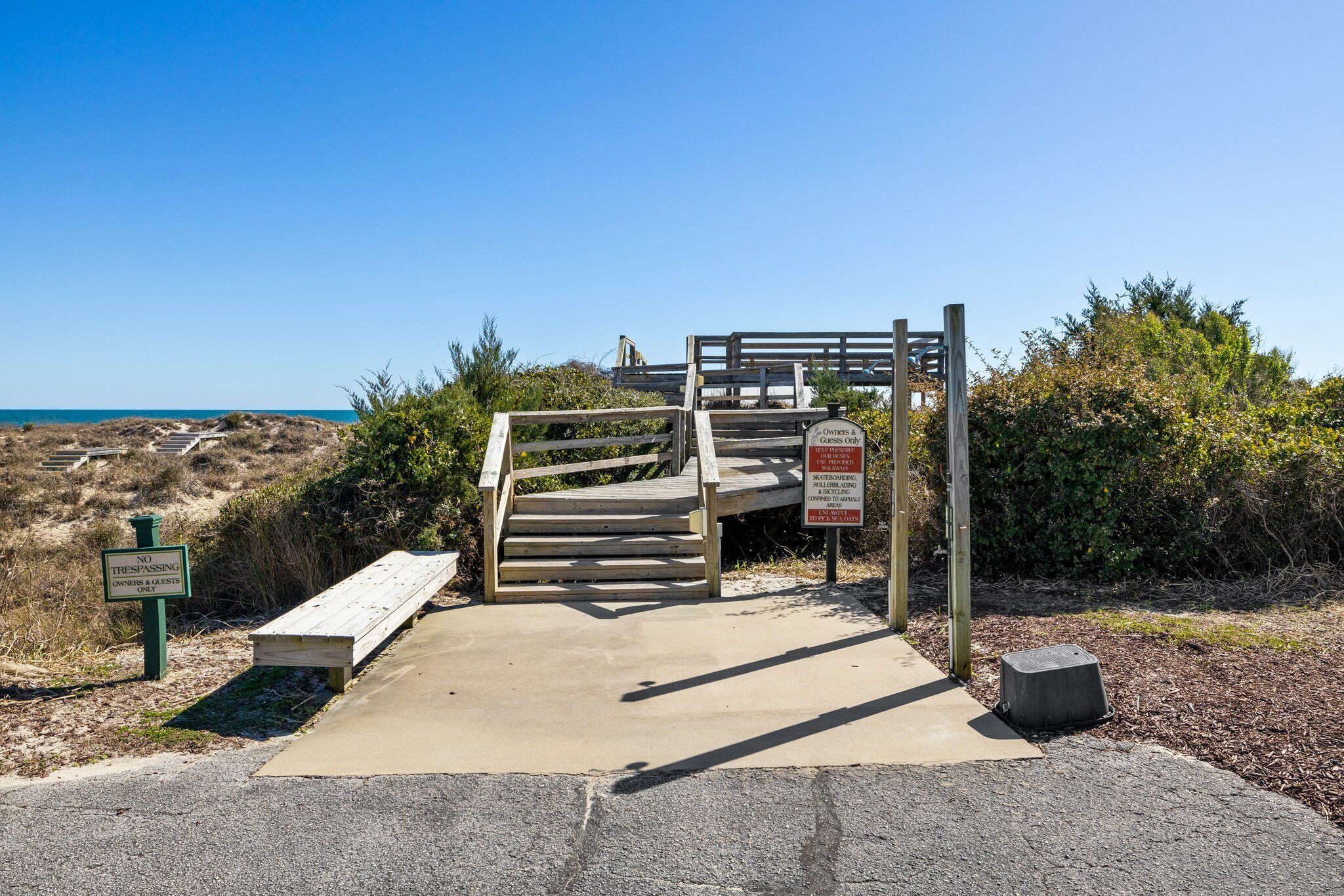 A wooden staircase leading to a beach area with a 'No Trespassing' sign and a sign indicating 'Owners & Guests Only' with restricted activities.