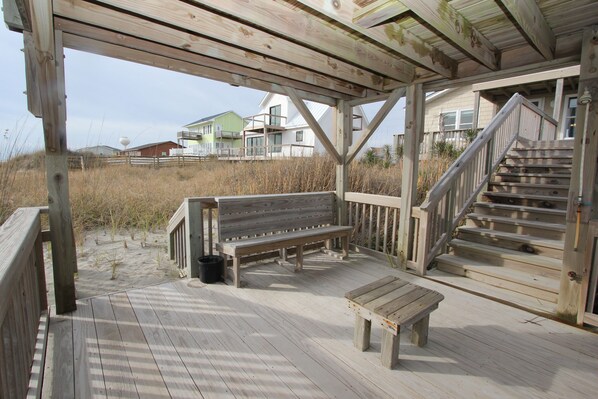 A wooden deck with a bench and a table, a staircase, and a view of houses in the background. - 4BR, Ocean Front, Dogs OK - One Level! (Emerald Isle)