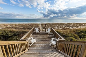 Eine Holzterrasse mit weißen Stühlen mit Blick auf einen Strand.