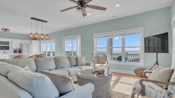 A spacious living room with a large sectional sofa, a round coffee table, and a ceiling fan. - Pool & Hot Tub- DOGS OK! 5BR w/ Ocean Views! (Emerald Isle)
