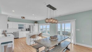 A spacious kitchen with white cabinets, a wooden dining table, and a view of the ocean. - Pool & Hot Tub- DOGS OK! 5BR w/ Ocean Views! (Emerald Isle)