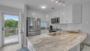 A modern kitchen with white cabinets, a stainless steel refrigerator, a microwave, and a large island with a sink. - Sound of the Sea 203N - 2BR Condo w/ Pool! (Emerald Isle)