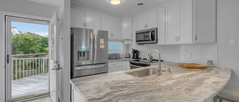 A modern kitchen with white cabinets, a stainless steel refrigerator, a microwave, and a large island with a sink.