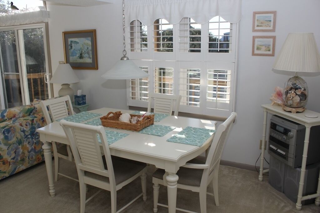 A dining area with a white table and chairs, a basket of bread, and a lamp on a side table.