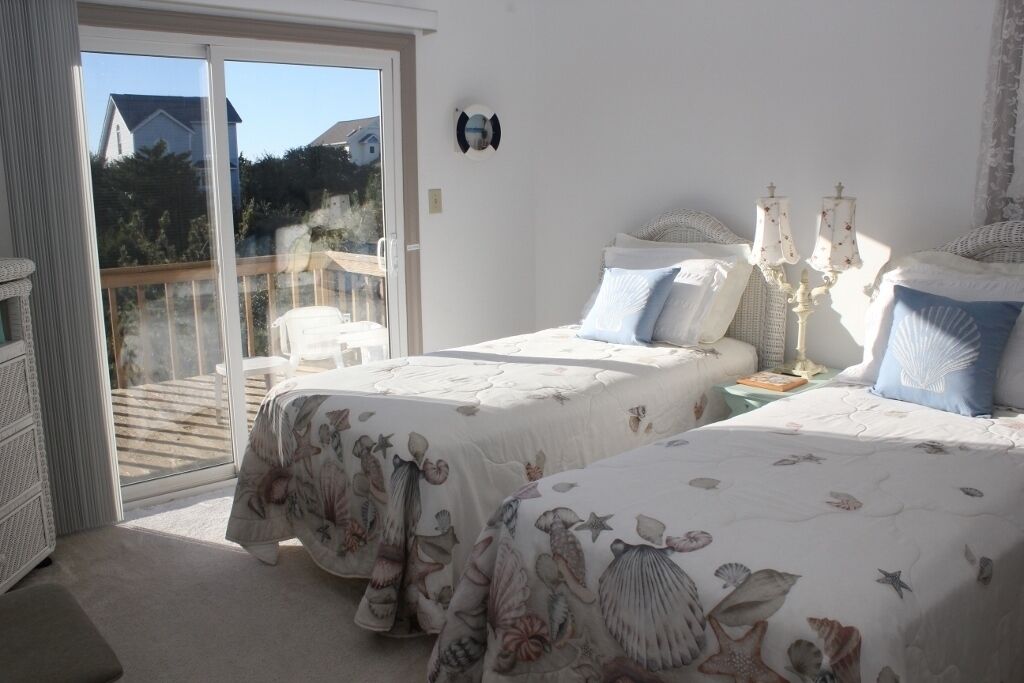 A bedroom with two beds, a balcony, and a white wall.