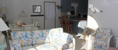 A living room with a floral sofa, a glass coffee table, and a dining area with chairs.