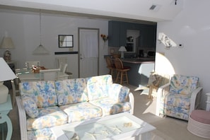 Uma sala de estar com um sofá floral, uma mesa de centro de vidro e uma área de jantar com cadeiras.