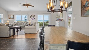 A spacious living area with a wooden dining table, two sofas, a ceiling fan, and a view of the ocean. - POOL & DOGS WELCOME! Easy Beach Access (Emerald Isle)
