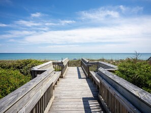 Eine Holzpromenade, die zu einem Strand führt, mit freiem Blick auf den Ozean.