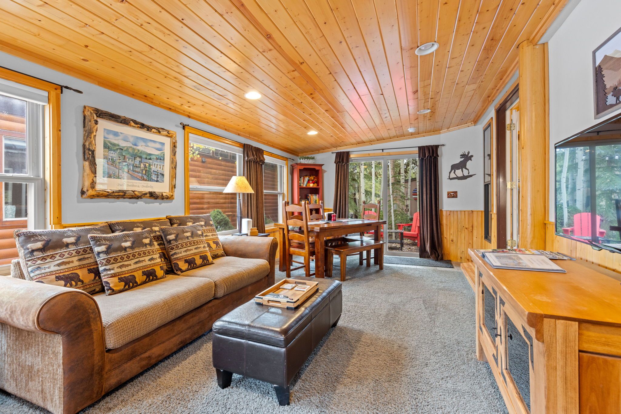 Interior acogedor de una cabaña con techo de madera, un sofá con cojines estampados, una mesa de comedor y una chimenea.