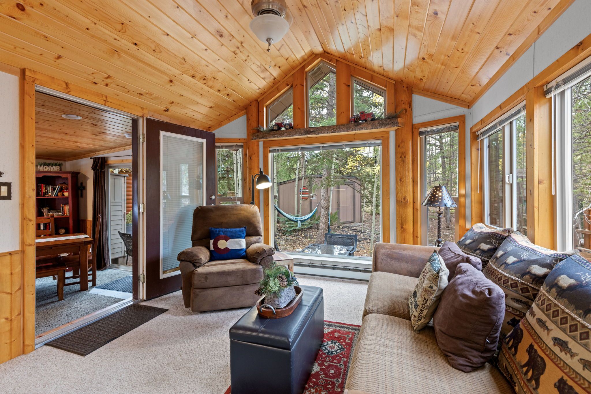 A cozy living room with a fireplace, a large window, and a wooden ceiling.