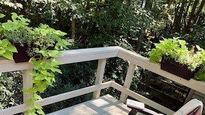 En træterrasse med et bord og stole, omgivet af frodig vegetation.