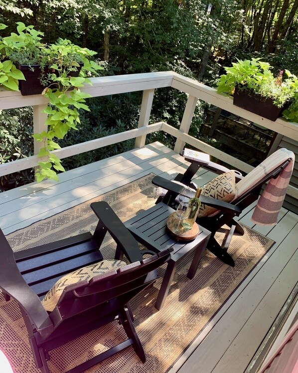 A wooden deck with a table and chairs, surrounded by lush greenery.