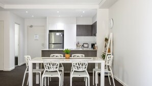 Une cuisine moderne avec des meubles blancs, un réfrigérateur en acier inoxydable et un petit îlot central doté d’un grille-pain et d’un évier.