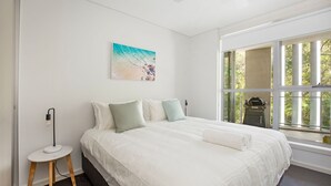Une chambre avec un grand lit, une petite table de chevet, une lampe fixée au mur et une fenêtre donnant sur un paysage verdoyant.