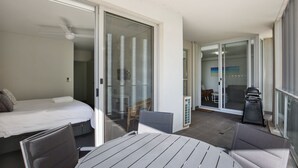 Une pièce comprenant un lit, une table et une chaise. Une porte-fenêtre coulissante donne sur un balcon où se trouvent une chaise et une table.