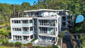 Un immeuble moderne à plusieurs étages, doté de balcons, portant l’inscription « Aquamist », et entouré d’une végétation luxuriante.