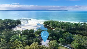 An aerial view of a coastal area with a beach, dense greenery, and a clear blue sky. - Bay Blu - Pet Friendly - Waterfront (Huskisson)