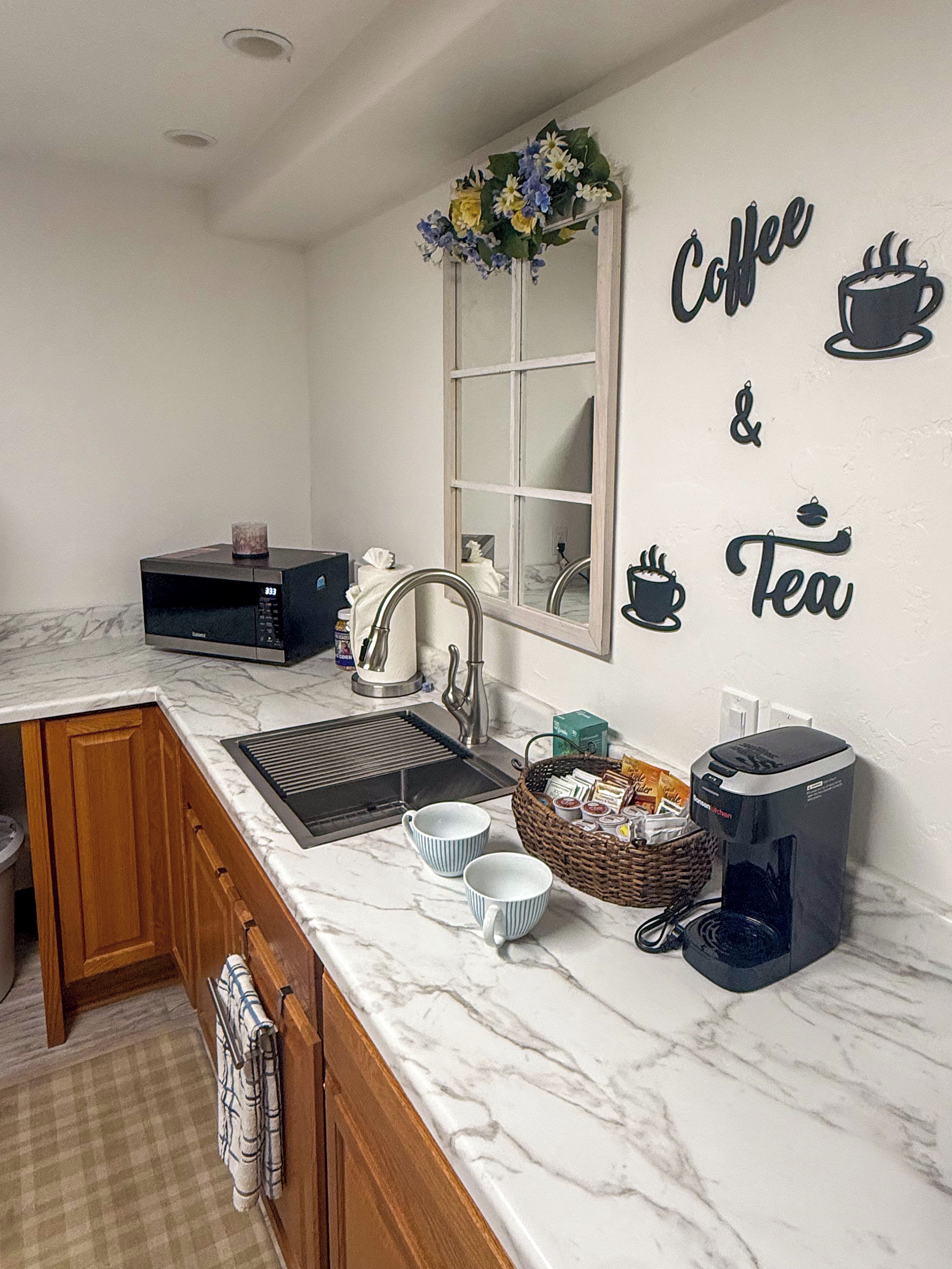 A kitchen with a marble countertop, a coffee maker, a microwave, and a wall decoration that reads 'Coffee & Tea'.