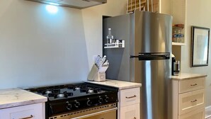 Een moderne keuken met een roestvrijstalen fornuis, oven en koelkast, houten vloeren en witte kastjes.