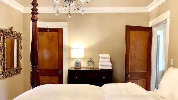 Een hotelkamer met een hemelbed, een kroonluchter, een houten dressoir en een spiegel aan de muur.