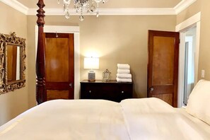 Une chambre d’hôtel avec un lit à baldaquin, un lustre, une commode en bois et un miroir au mur.