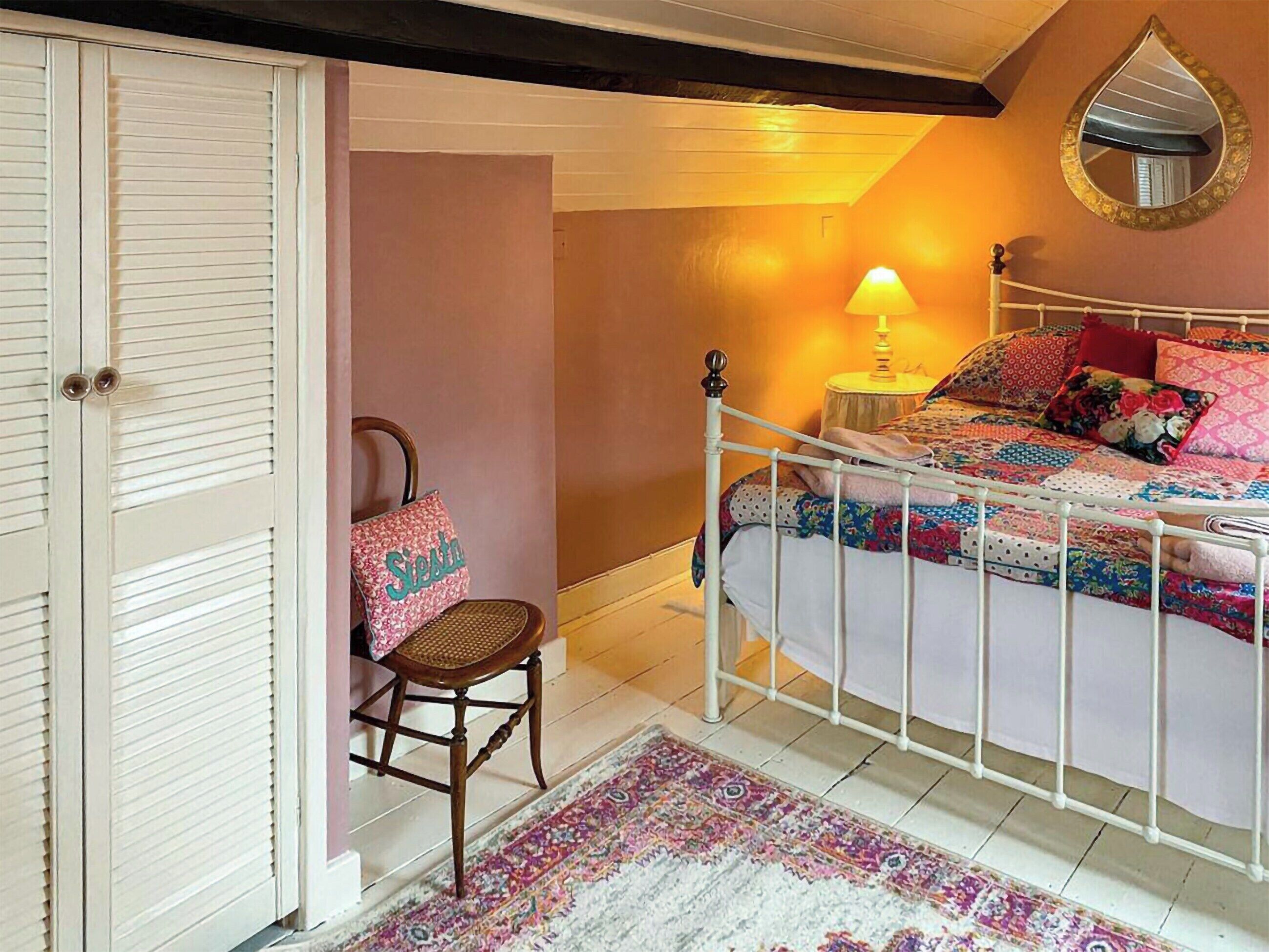 A bedroom with a bed, a chair, a nightstand, a lamp, and a mirror.