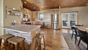 Une cuisine spacieuse avec des meubles en bois, un grand îlot central et un mur d’accent en pierre.