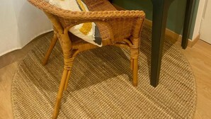 Une chaise en osier avec un coussin, un bureau avec une lampe et un tapis tissé.