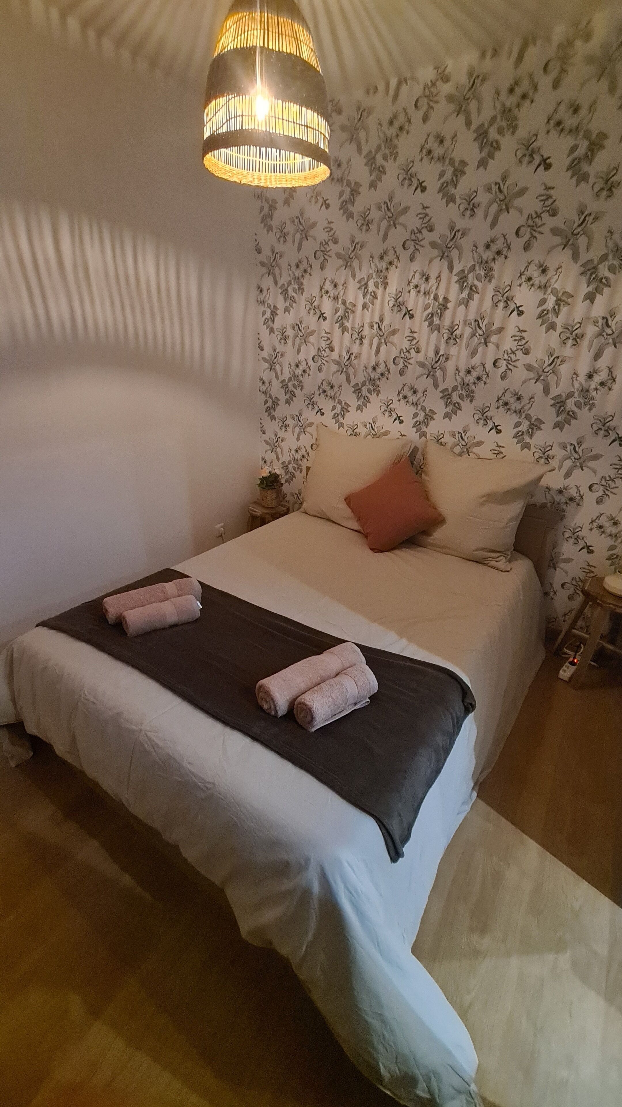 Un dormitorio con cama, almohadas, una colcha, lámpara colgante y papel tapiz floral.
