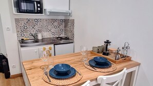 Une cuisine compacte avec des meubles blancs, un four à micro-ondes et une cuisinière. On y trouve une table à manger en bois, avec des assiettes bleues et un verre.
