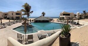 A pool area with lounge chairs and umbrellas, surrounded by palm trees and a view of the beach. - Terrasol Beach Resort, Oceanfront 2BR Condo #106 (Cabo San Lucas)