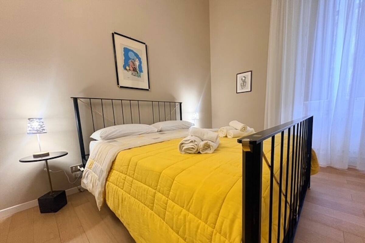 Une chambre d’hôtel avec un lit, une petite table avec une lampe et une fenêtre avec des rideaux.
