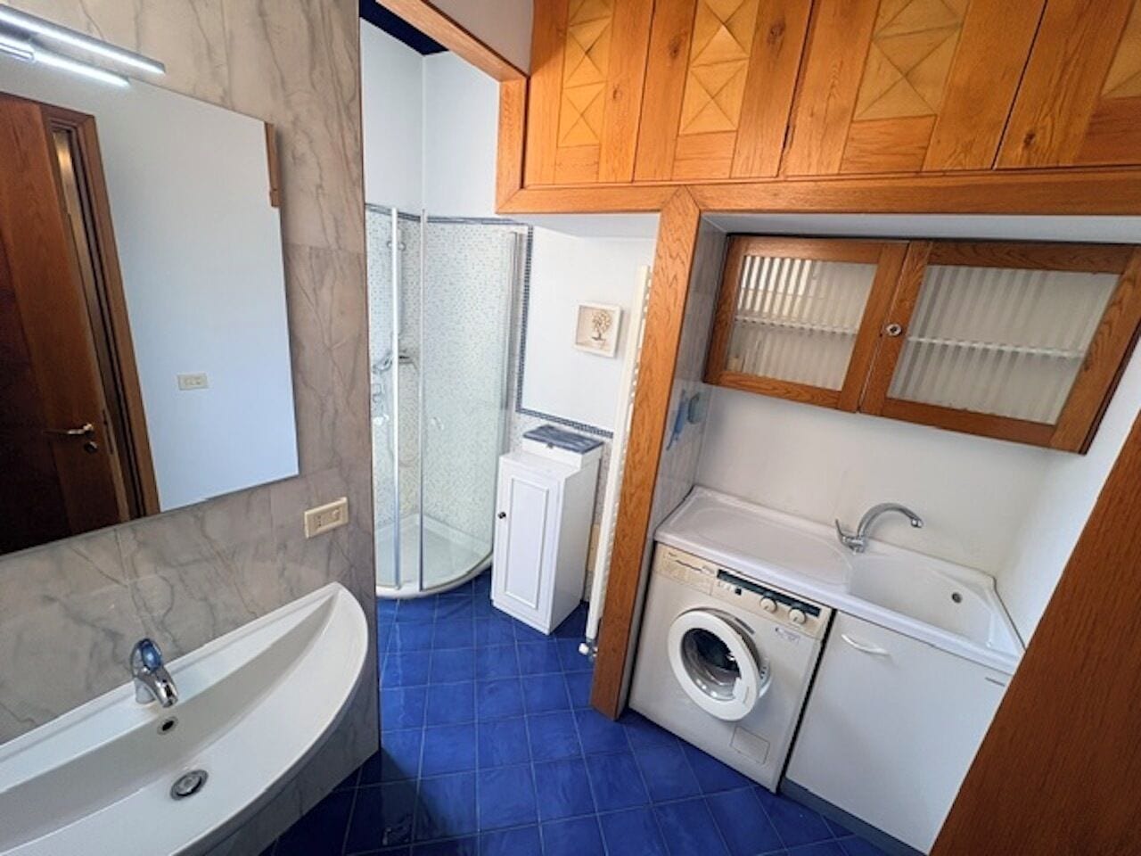 Ein kleines Badezimmer mit Waschbecken, Spiegel, Dusche und Waschmaschine.